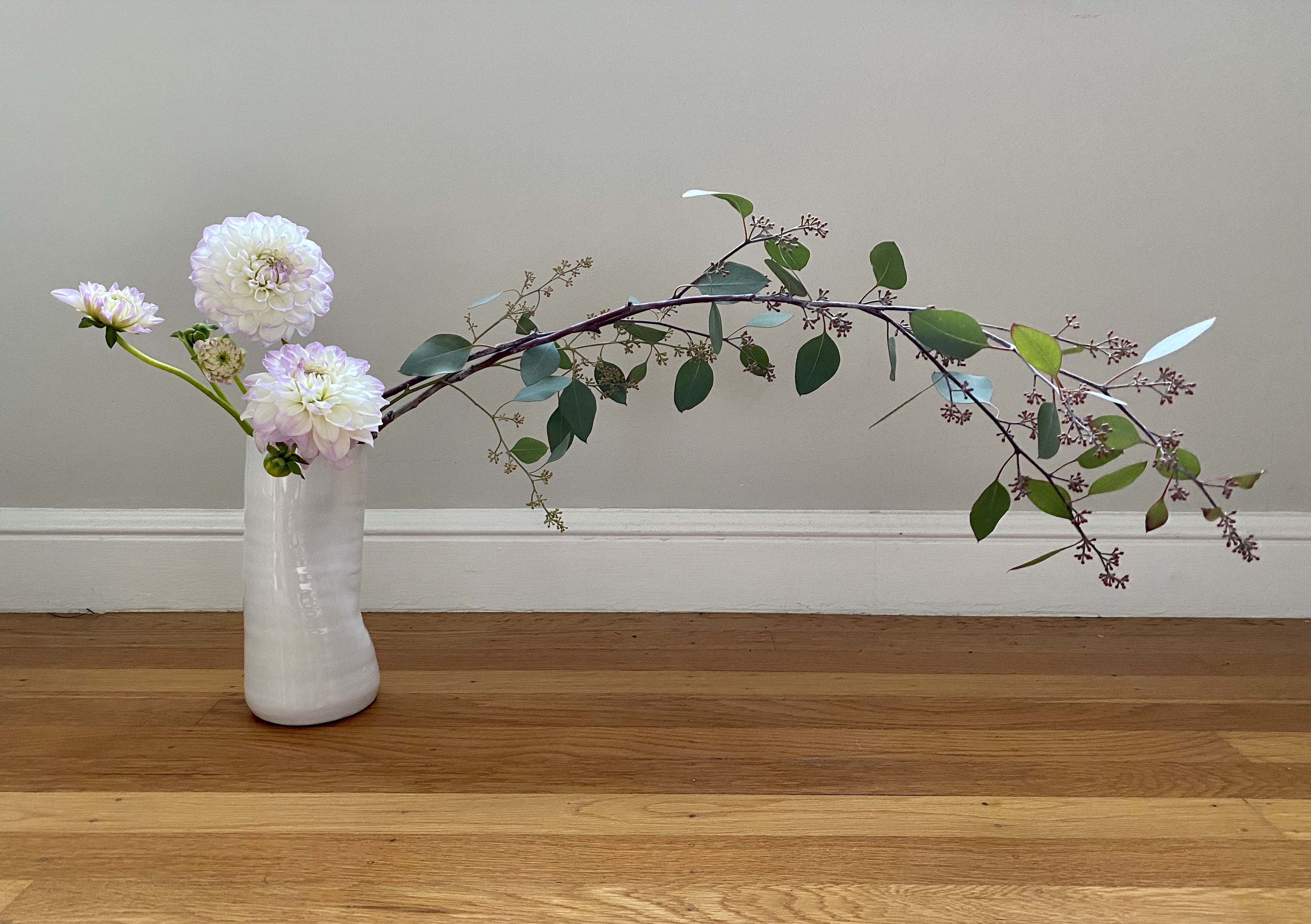 Dahlias and eucalyptus arranged horizontally, in a white hand molded vase