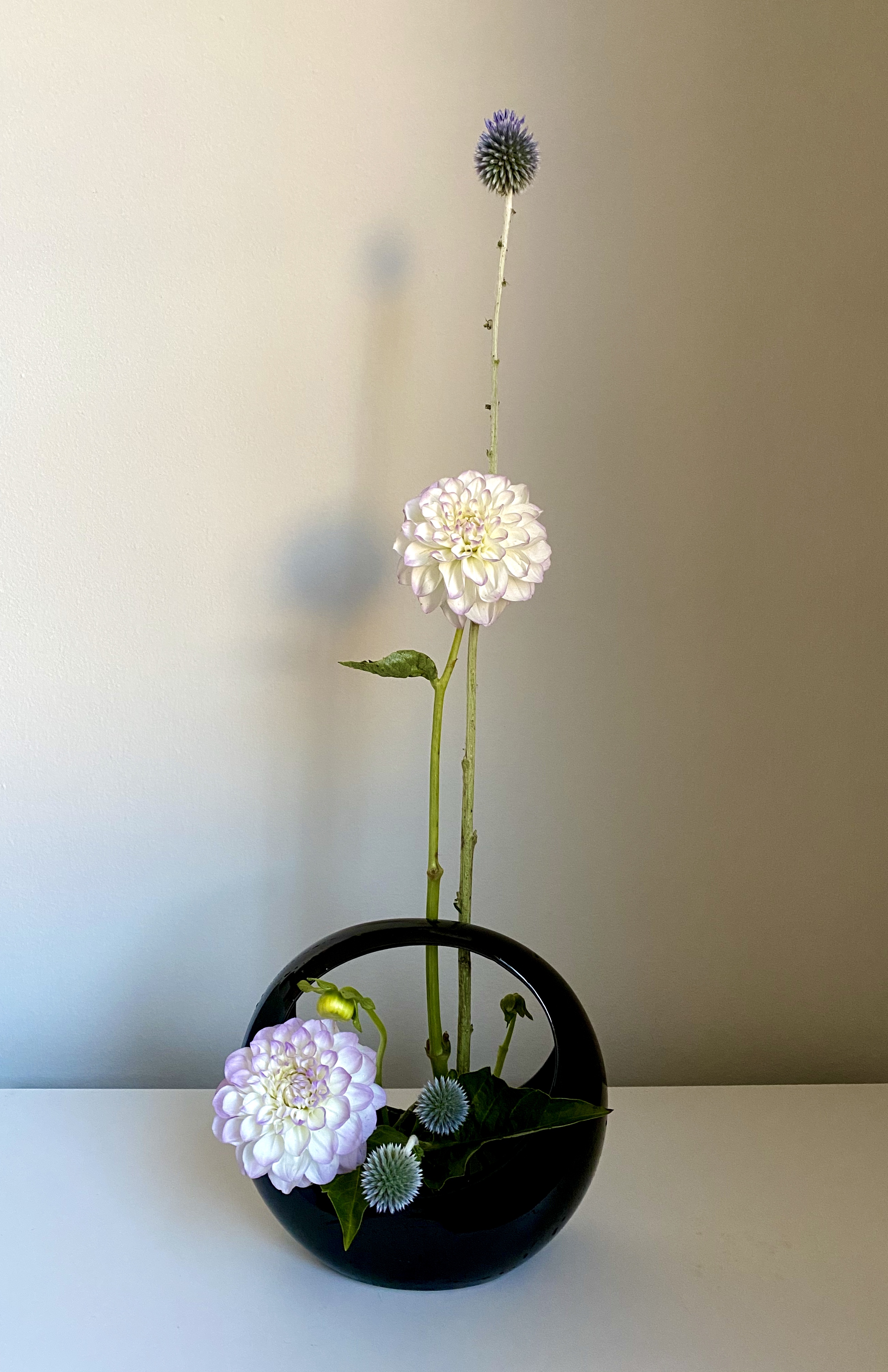 Thistles and dahlias arranged in an elliptical vase, with a hole in the middle of it