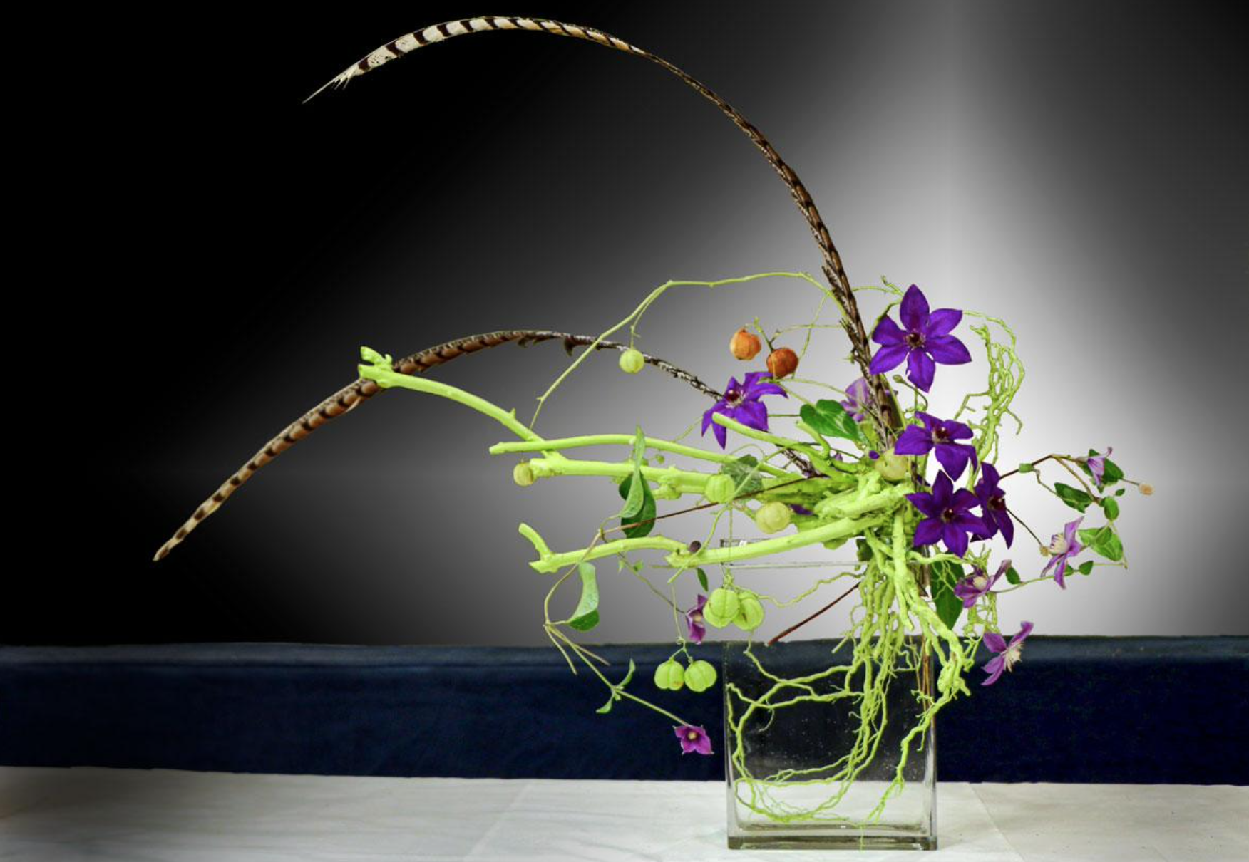A floral arrangement featuring purple orchids and spindly green foliage, in a clear, rectangular vase