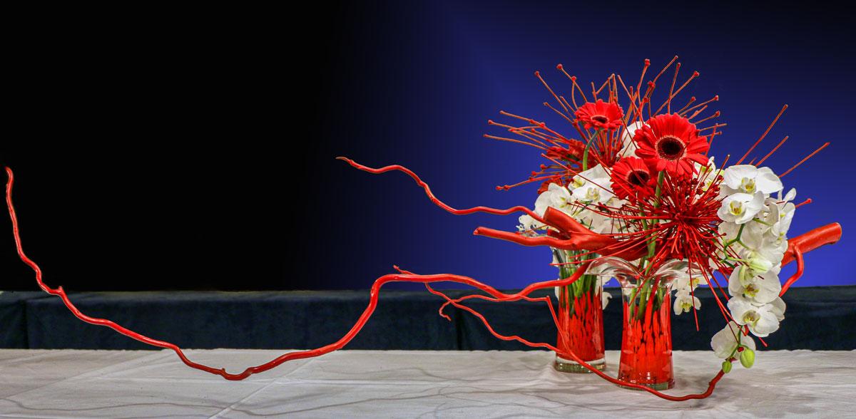 A floral arrangement made from two red vases, tree branches painted red, orchids, and red flowers