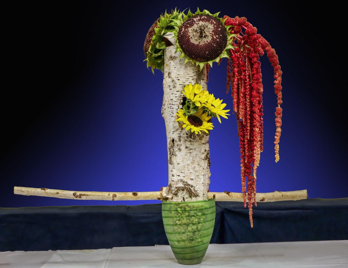 A floral arrangement made from a tree trunk, sunflowers and draping red flowers